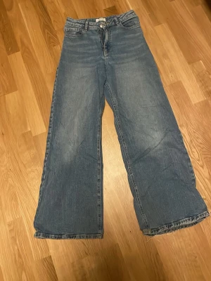 Blåa wide leg jeans från Lindex - Säljer ett par blåa wide leg jeans från Lindex med hög midja och klassisk femficksmodell. Jeansen har en avslappnad passform och är tillverkade i denim med snygg tvättad look. Perfekta för en trendig och bekväm stil.