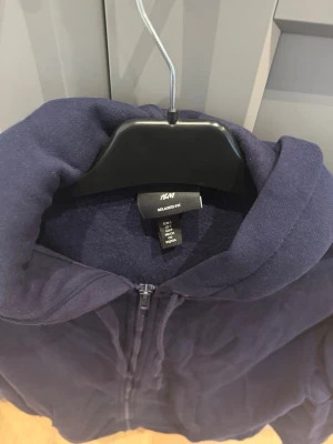 Mörkblå hoodie med dragkedja H&M - Mörkblå hoodie från H&M i relaxed fit med dragkedja framtill och två fickor. Tillverkad i mjuk bomullsblandning och har en stor huva. Perfekt för en chill och avslappnad stil.