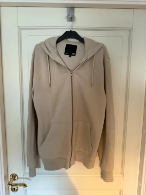 Beige hoodie med dragkedja från 157 - Säljer en beige hoodie från 157 med dragkedja framtill, två stora fickor och med huva. Skriv till mig vid undringar och pris kan diskuteras. Hämtas i Torslanda eller så fraktar jag.