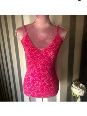 Rosa blommig linnetopp - Snygg rosa linnetopp med tunna axelband och blommigt mönster. Toppen har en v-ringad halsringning och är figurnära i modellen. Perfekt för varma dagar eller som layering-plagg. Med inbyggd bh 