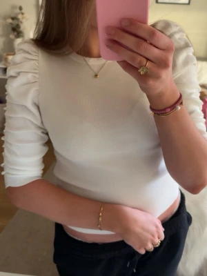 Vit topp - Snygg vit ribbad topp med puffade, rynkade ärmar i trekvartslängd. Figurnära passform och rund halsringning🤍