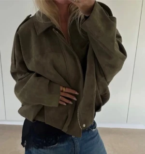 Zara suede bomberjacket - Säljer en olivgrön oversized mockajacka med dragkedja framtill och bred krage. Jackan har långa ärmar och en loose passform som ger en chill vibe. Materialet är mjuk mocka och färgen är matt olivgrön. Perfekt för dig som gillar streetstyle och vill ha något som sticker ut.