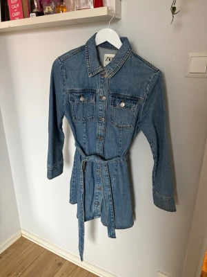 Långärmad jeansklänning storlek S/M - Jättefin långärmad jeansklänning med knyt/band i midjan och knappar längs ner mitten. Skulle säga att den passar S/M. Tidslös och perfekt till vår/sommar/höst!! 100% bomull och inga defekter. Kom gärna med prisförslag 🌸 går ner i pris vid snabbt köp!