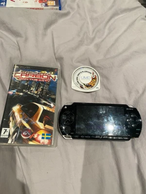 Sony PSP svart spelkonsol - Säljer en svart Sony PSP spelkonsol med tillhörande spel. Medföljer UMD-skivor FIFA Street 2. Konsolen har klassisk design med knappar på sidorna och stor skärm i mitten. Perfekt för dig som gillar portabel gaming 8gb utrymme plus en laddare ingår inte med på bild original laddare.