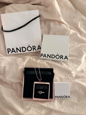 Pandora halsband & ring hjärta röd - Säljer ett matchande smyckeset från Pandora med halsband och ring. Båda har ett hjärtformat rött hänge/sten och är i silverfärgat material. Perfekt för dig som gillar romantiska detaljer och stilrena accessoarer. Kommer i originalförpackning.