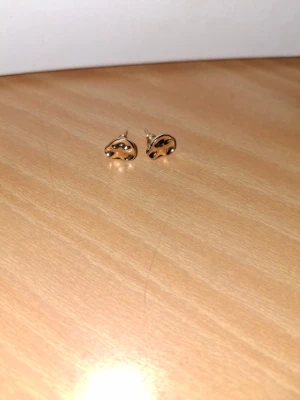 Guldiga örhängen i abstrakt form - Säljer ett par små, guldiga örhängen med en cool abstrakt design. De är i metall och har en unik, organisk form som sticker ut. Perfekta för dig som gillar minimalistiska men ändå speciella accessoarer.