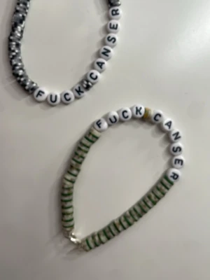Pärlarmband med text Fuck Cancer - Två handgjorda armband med vita pärlor som stavar 'FUCK CANCER'. Ett armband har svarta och vita pärlor, det andra har gröna och vita pärlor. Elastisk tråd gör dem enkla att ta på och av. Perfekt accessoar för att visa stöd och attityd. Finns i dessa färger också.❤️‍🩹 20kr st 2 för 35kr 