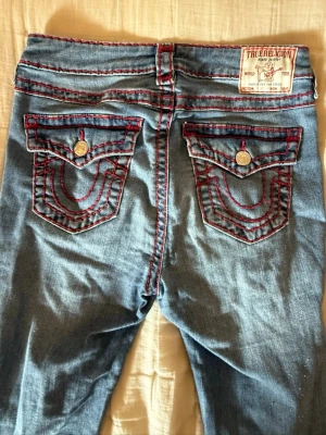Bootcut True Religion jeans med röd söm. ❤️❤️❤️ - ❤️❤️❤️Snygga blå jeans från True Religion med ikoniska bakfickor, röda kontrastsömmar och silverfärgade knappar. Klassisk femficksmodell i denim med tydliga detaljer och patch på linningen. Använda två gånger. Storlek s-m långa.