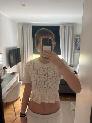 Vit stickad croppad topp med volang - Säljer en söt vit stickad topp med korta puffärmar och volangkant nedtill. Toppen har ett fint hålmönster. 