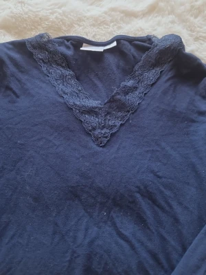 Marinblå topp med spets från Gina Tricot - Mysig marinblå topp från Gina Tricot med v-ringning dekorerad med spetsdetaljer. Perfekt för dig som gillar en enkel men ändå söt stil. Tunn och mjuk i materialet, passar till många olika outfits. Storleken är 170 och nästan alldrig använd!  