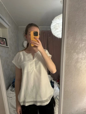 Vit blus med ficka från Fransa - Säljer en enkel och stilren vit blus från Franss. Blusen har korta ärmar, en bröstficka och en liten v-ringning med detalj framtill. Perfekt till jeans eller kjol för en clean look.