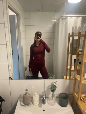 Vinrött träningsset med dragkedja - Säljer ett vinrött träningsset med långärmad zip-tröja och matchande yoga tights. Setet har en åtsittande passform och är gjort i ett stretchigt material som passar perfekt för gymmet eller löpning. Tröjan har hög krage och hel dragkedja framtill.   Hela setet 370, annars 220kr styck 