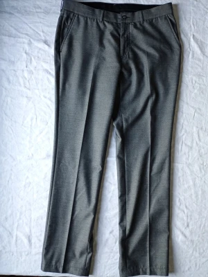 Grå kostymbyxor med pressveck - Snygga grå kostymbyxor med klassiskt pressveck och raka ben. Byxorna har sidfickor och bälteshällor i midjan. Perfekta för en stilren och clean look. Materialet känns mjukt och har en lätt glansig finish.