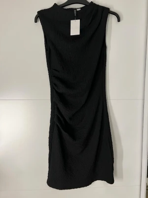 Svart  klänning från H&M - Stilren svart ärmlös klänning från H&M med strukturerat tyg och rak passform. Klänningen har en enkel design med hög hals och är perfekt för dig som gillar minimalistisk stil.