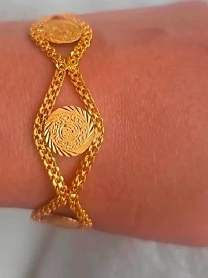 Guldarmband med myntdetaljer - Snyggt armband i guldfärgad metall med flera tunna kedjor som korsar varandra och runda myntliknande detaljer med ingraverat mönster. Perfekt accessoar för dig som gillar unika smycken med lite extra bling.