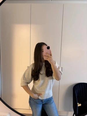 Beige stickad tröja med puffärm - Säljer en beige stickad tröja med korta puffärmar och rund hals. Tröjan har en avslappnad passform och ribbade muddar vid ärmslut och nederkant. Perfekt för dig som gillar en enkel men trendig look.