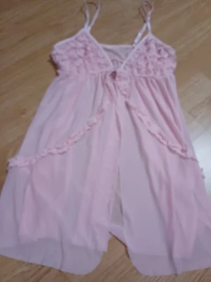 Ljusrosa nattlinne med volangdetaljer - Sött ljusrosa nattlinne med tunna axelband och volangdetaljer över bysten och längs framsidan. Tillverkat i ett tunt, transparent tyg som ger en romantisk och luftig känsla. Perfekt för mysiga kvällar hemma.