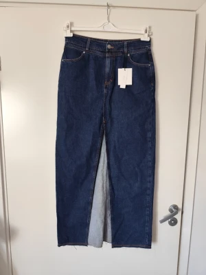 Mörkblå jeanskjol med slits - Rak, lång jeanskjol i mörkblå denim med hög midja och slits framtill. Klassisk femficksmodell med kontrastsömmar och knappgylf. Perfekt för dig som gillar en clean och tidlös look.