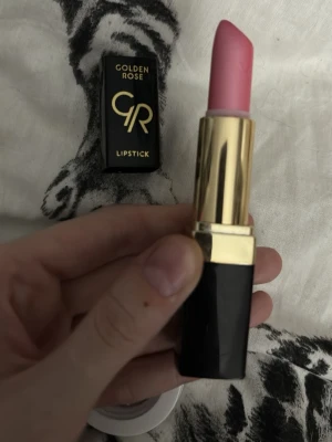 Rosa läppstift från Golden Rose - Snyggt rosa läppstift från Golden Rose med klassisk svart och guldig hylsa. Läppstiftet har en mjuk, krämig formula och ger en fräsch rosa färg till läpparna. Perfekt för dig som vill ha en poppig och feminin look.
