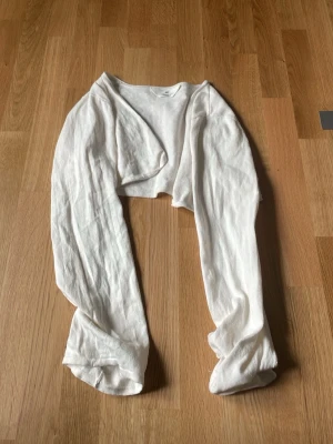 Vit cropped bolero med långa ärmar - Säljer en vit, tunn och mjuk cropped bolero med långa ärmar. Perfekt att slänga över ett linne eller klänning för en chill och stilren look. Materialet känns lätt och luftigt, vilket gör den skön att bära inomhus eller under vår och sommar.