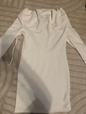 Vit långärmad kortklänning - Säljer en stilren vit kortklänning med långa ärmar och en snygg draperad krage. Klänningen har en figurnära passform. Tajtare nere och lösare runt bysten. Nypris 200kr 
