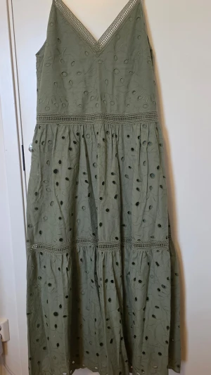 Ivy & Oak olivgrön långklänning med broderade detaljer - Snygg grön långklänning med v-ringning och breda axelband. Klänningen har broderade hålmönster och spetsdetaljer vid midjan och kjolen. Tillverkad i bomull, perfekt för varma dagar och somriga tillfällen.