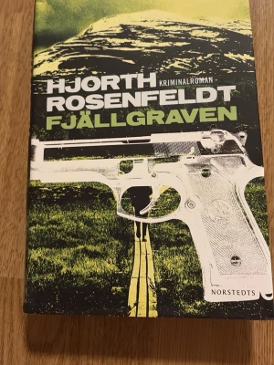 Fjällgraven av Hjorth, Rosenfeldt - Kriminalroman med svart och grön omslagsdesign, motiv av fjäll, pistol och en person på en stig. Skriven av Hjorth och Rosenfeldt och utgiven av Norstedts. Tredje boken om Sebastian Bergman och Riksmord. Perfekt för dig som gillar spänning och deckare.