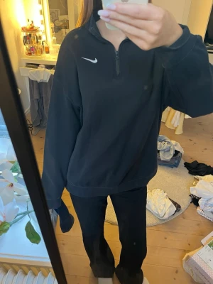 Svart Nike sweatshirt med halvzip - Svart sweatshirt från Nike med halv dragkedja och hög krage. Tröjan har relaxed fit, långa ärmar och en vit Nike-logga på bröstet. Tillverkad i mjukt material som ger en chill och sportig vibe.