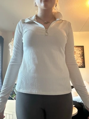 Vit ribbad polotopp med half zip - Vit ribbad polotopp med lång ärm och half zip framtill. Toppen har en tight passform och hög krage som kan vikas ner. Perfekt för en clean och stilren look.