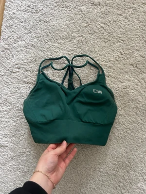 Grön sport-bh från ICIW - Mörkgrön sport-bh från ICIW med korsade band. Väldigt bekväm och ger bra stöd. Loggan framtill är i vit text och bak är den mer diskret. Använd fåtal gånger.