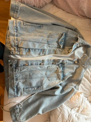 Ljusblå oversized jeansjacka - Säljer en ljusblå oversized jeansjacka med klassisk krage, knappstängning framtill och två bröstfickor med lock. Jackan har raka ärmar och en avslappnad passform som ger en cool och trendig look. Perfekt att slänga över en hoodie eller t-shirt.