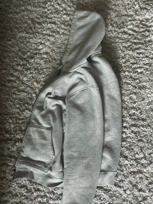 Grå hoodie med Burberry-mönstrad huva - Säljer en grå hoodie med dragkedja från Burberry. Utsidan är enkel och stilren medan insidan av huvan har det klassiska Burberry-rutiga mönstret i beige, svart, vitt och rött. Hoodien har fickor framtill och ribbade muddar.