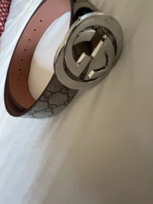  GG bälte  - Snyggt  GG  bälte med klassiskt monogrammönster och stor silverfärgad dubbel-G-spänne. Bältet är beige och brunt med insida i ljusrosa läder. Perfekt accessoar för att lyfta din outfit.