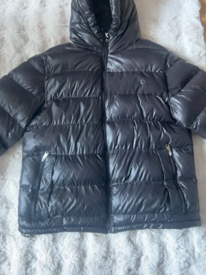 Svart pufferjacka från Alessandro - Tvär snygg jacka från Allesandro zavetti med glansigt material. Jackan är i väldigt bra skick och finns inga defekter förutom att texten/bokstväverna på bröstet sitter lite löst och har lossnat lite. Jackan har många feta detaljer, finns värmefickor och vanliga. Skicka ett prisförslag om priset inte skulle duga! Skickar så snabbt jag kan! Storlek XL