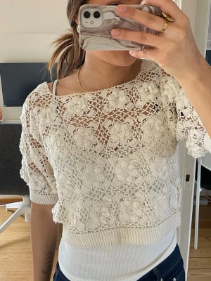 Vit spetsblus med blommönster - Säljer en superfin vit blus i spets med blommigt mönster och korta ärmar. Blusen är croppad och har ribbade kanter nedtill och vid ärmsluten. Perfekt för dig som gillar romantisk och söt stil.