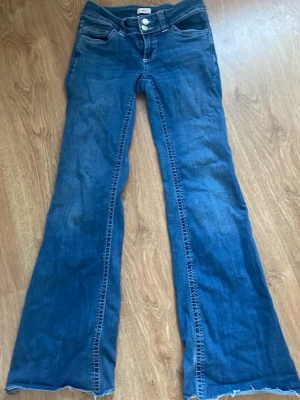 Blå bootcut jeans från Nelly - Säljer ett par blå bootcut jeans från Nelly med klassiska fickor och snygga broderade detaljer på bakfickorna. Jeansens kanter är avklippta längst ner men perfekt längd för mig som är 162, och är tillverkade i denim. Perfekt för dig som gillar en avslappnad och trendig stil.