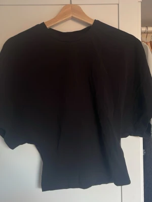 Svart t-shirt från Nelly - En svart t-shirt från Nelly som går in i midjan och har en lös passform upptill, den har klassisk rund hals och korta ärmar. Perfekt till jeans eller kjol och enkel att styla med olika accessoarer.