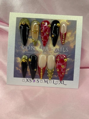 Baddie (S);Medium Stiletto - Unika handgjorda press-on naglar i svart, guld, rött och nude. Medium långa, spetsiga stilettformade naglar dekorerade med guldiga pärlor och detaljer. Några naglar har röd nailart och andra är helsvarta eller nude med french. Perfekt för dig som vill sticka ut!S: 15 mm, 11,5 mm, 12 mm, 11 mm, 9 mm 