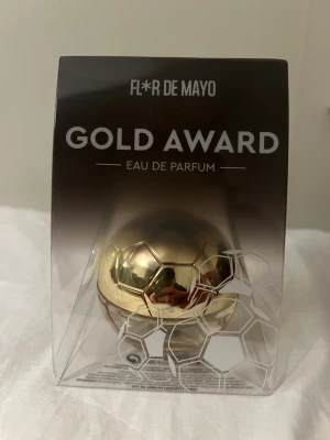 Flor de Mayo Gold Award Parfym - Unik parfym från Flor de Mayo i en cool guldfärgad bollformad flaska, inspirerad av en fotboll. Flaskan är tillverkad i glas och plast med metallisk finish. Doften är Eau de Parfum och förpackningen har en modern sportig design.