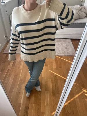Randig stickad tröja i offwhite och svart - Säljer en oversized stickad tröja i offwhite med breda svarta ränder. Tröjan har rund halsringning, långa ärmar och ribbade muddar vid ärmslut och nederkant. Perfekt för en avslappnad och trendig look.