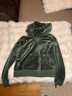 Grön velour  från Juicy Couture Dress  - Mjuk och skön hoodie i grön velour från Juicy Couture. Dragkedja framtill, två fickor och broderad logga på bröstet. Klassisk huva och ribbade muddar vid ärmslut och nederkant. Perfekt för en chill och trendig look.