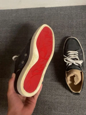 Christian Louboutin BYTES! - Tja lägger ut dessa skor och ser ifall någon har något erbjudande i byte mot mina loubutin, dem här är Snygga svart grå sneakers med vit snörning och ikonisk röd sula. Skorna har en klassisk låg profil och vita detaljer runt sulan. Perfekta för dig som vill sticka ut med en unik detalj under foten.