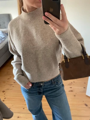 & other stories stickad tröja  - Säljer en beige stickad tröja med hög krage och långa ärmar. Tröjan har en avslappnad passform och är gjord i ett mjukt material som känns skönt mot huden. Perfekt att styla med jeans för en enkel och snygg look.