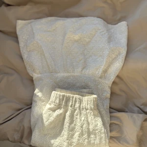 Vit långkjol  med blommönster - Vit långkjol i spets med blommigt mönster och elastisk midja. Kjolen är lätt och luftig, och har en underkjol så den är inte genomskinlig. Nypris 800kr.