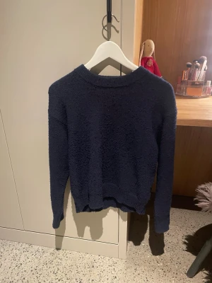 Mörkblå stickad tröja Gina Tricot - Mysig mörkblå stickad tröja från Gina Tricot i fluffigt material. Tröjan har rund halsringning, långa ärmar och en avslappnad passform. Perfekt för kalla dagar och enkel att matcha med jeans eller kjol.