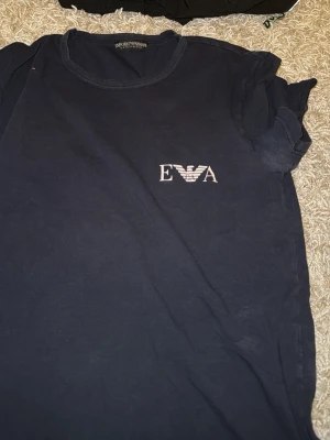 Mörkblå t-shirt Emporio Armani - Mörkblå t-shirt från Emporio Armani Underwear med vit EA-logga på bröstet. Klassisk rund halsringning och korta ärmar. Tillverkad i mjukt material som känns bekvämt mot huden. Perfekt för en avslappnad stil.