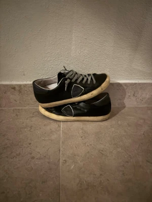 Svarta phillipe model skor - Säljer ett par svarta Philippe Model sneakers med grå snörning och vit sula. Skorna har en rund tå och är tillverkade i skinn med en snygg detalj på sidan. Perfekta för dig som gillar stilrena och klassiska sneakers. Stl 38