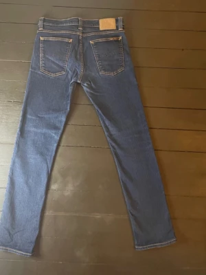 Blå Nudie jeans Tube Kelly - strl 29/32 - Säljer ett par Nudie Jeans av modell Tube Kelly i storlek 29/23, de är dock lite kortare så kolla måtten nedan. Byxorna är i mycket bra skick. Innerbenslängden är 73 cm, midjan har 74 cm i omkrets och benöppningen är 32 cm i omkrets. 