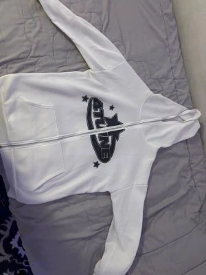 Vit hoodie med 4TUNE-tryck - Säljer en vit hoodie med dragkedja från 4TUNE. Hoodien har ett stort svart tryck med stjärnor på bröstet, två fickor framtill och en klassisk huva. Perfekt för dig som gillar streetwear och vill ha en enkel men snygg look.