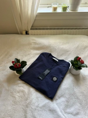 Mörkblå t-shirt från Stone Island - Snygg mörkblå t-shirt från Stone Island med klassisk rund hals och logopatch på bröstet. T-shirten är kortärmad och tillverkad i mjuk bomull, perfekt för dig som vill ha en stilren och trendig look.